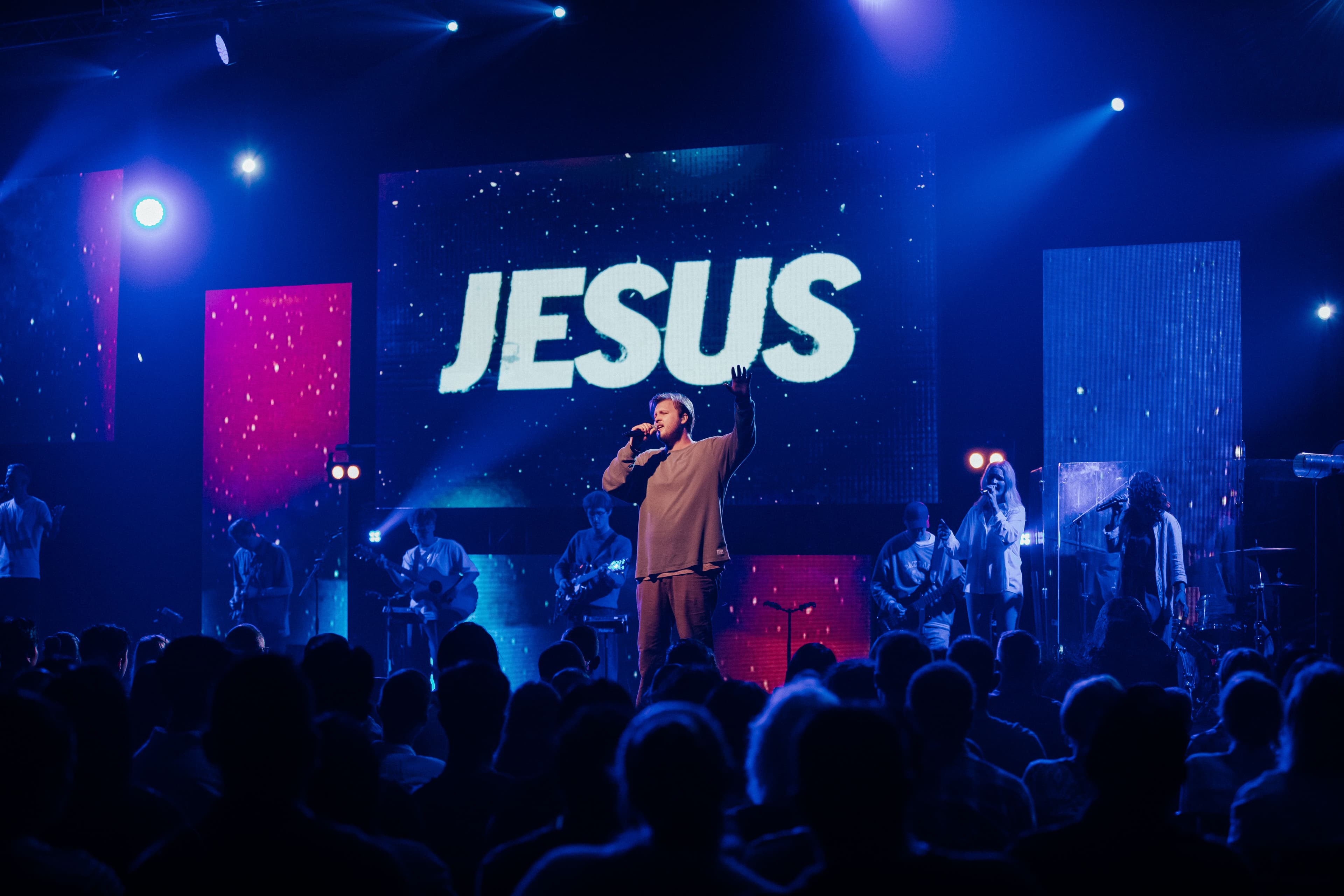 Man singing on stage with JESUS behind him on the screen