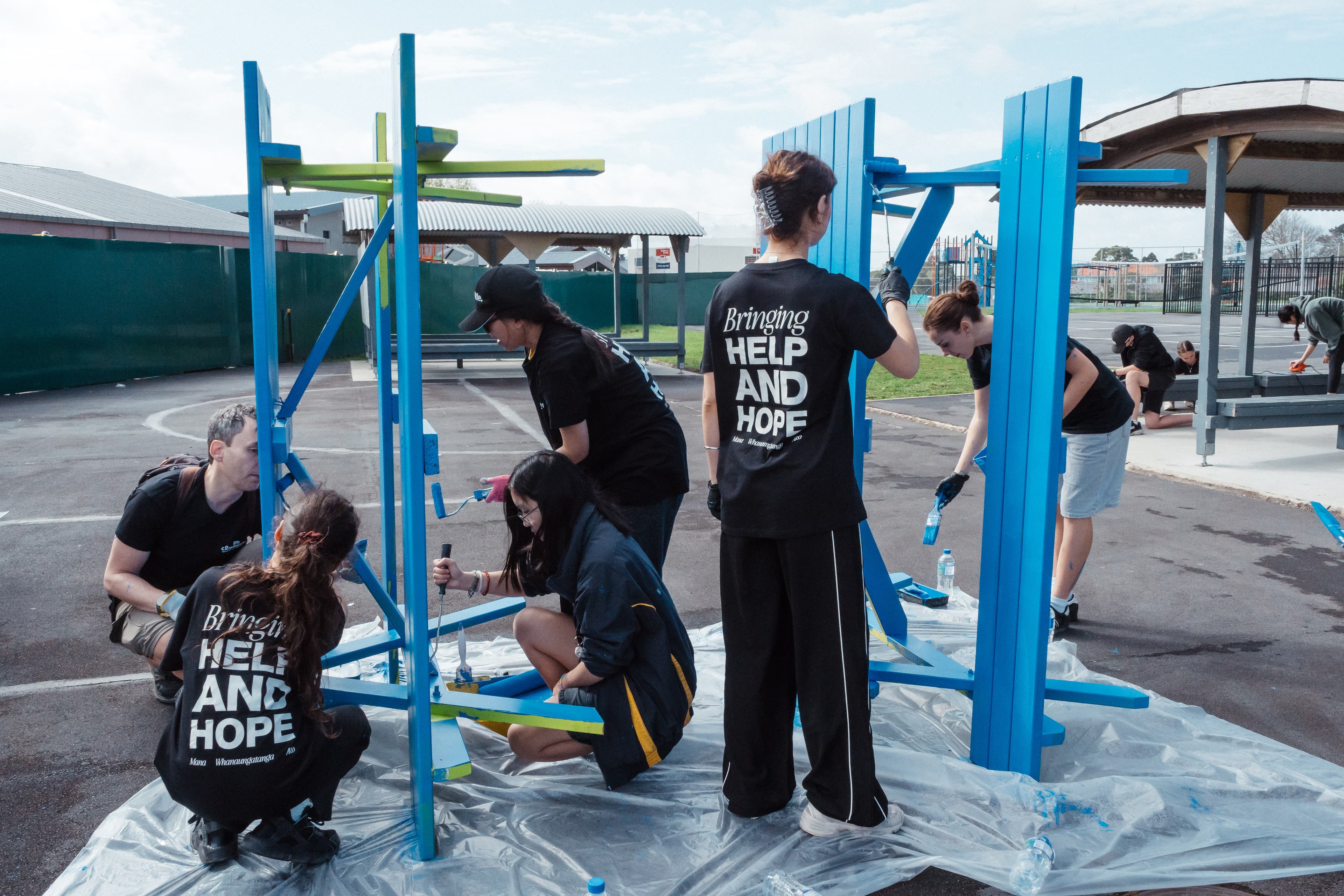 Group of volunteers paining picnic tables at a school for Help & Hope Week in matching t-shirts