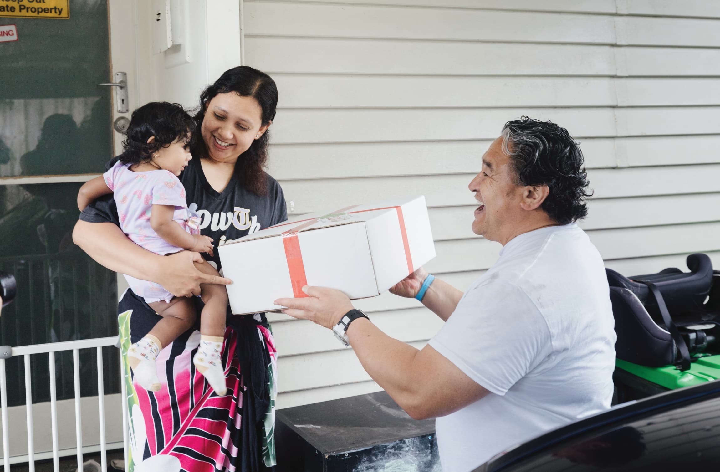 Man handing a Christmas Box to a woman holding a small child and smiling