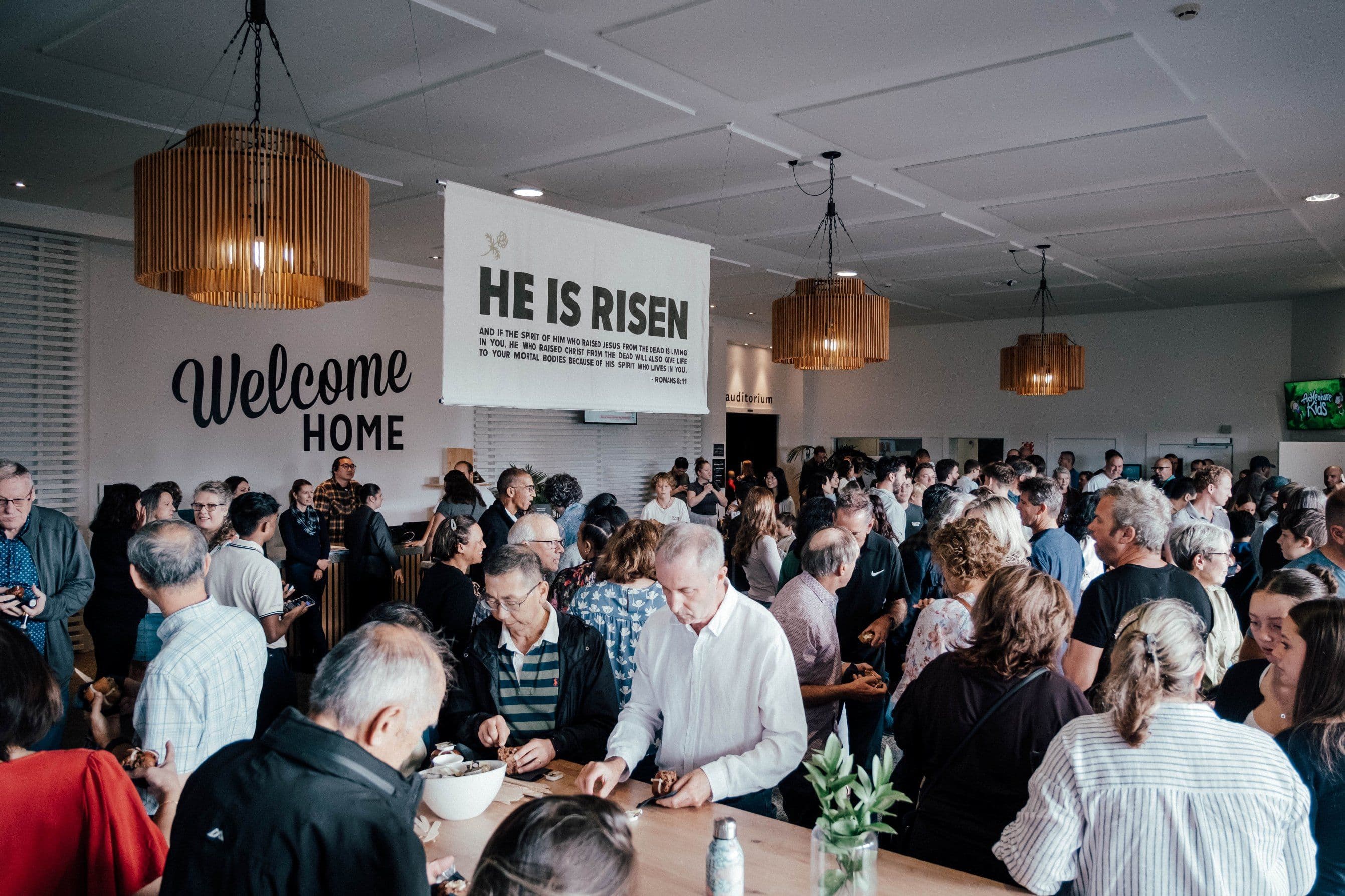 Wide shot of the foyer at North Campus on Good Friday with an Easter banner saying HE IS RISEN and people eating hot cross buns
