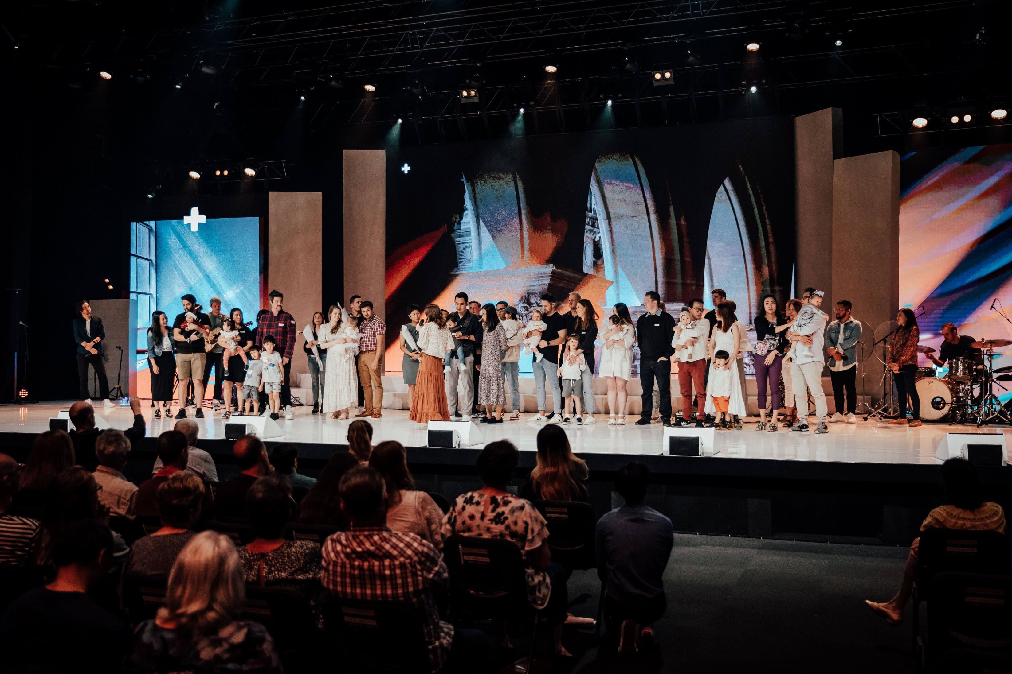 Lots of parents with their young children on the stage at Central campus with pastors behind them to pray for their children on Child Dedications day