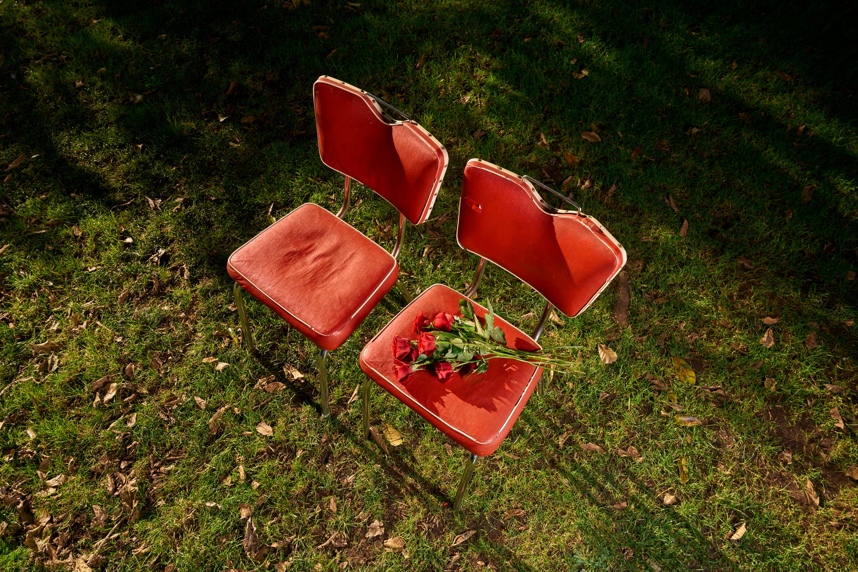 Two red chairs on grass with a bouquet of roses on the right-hand chair