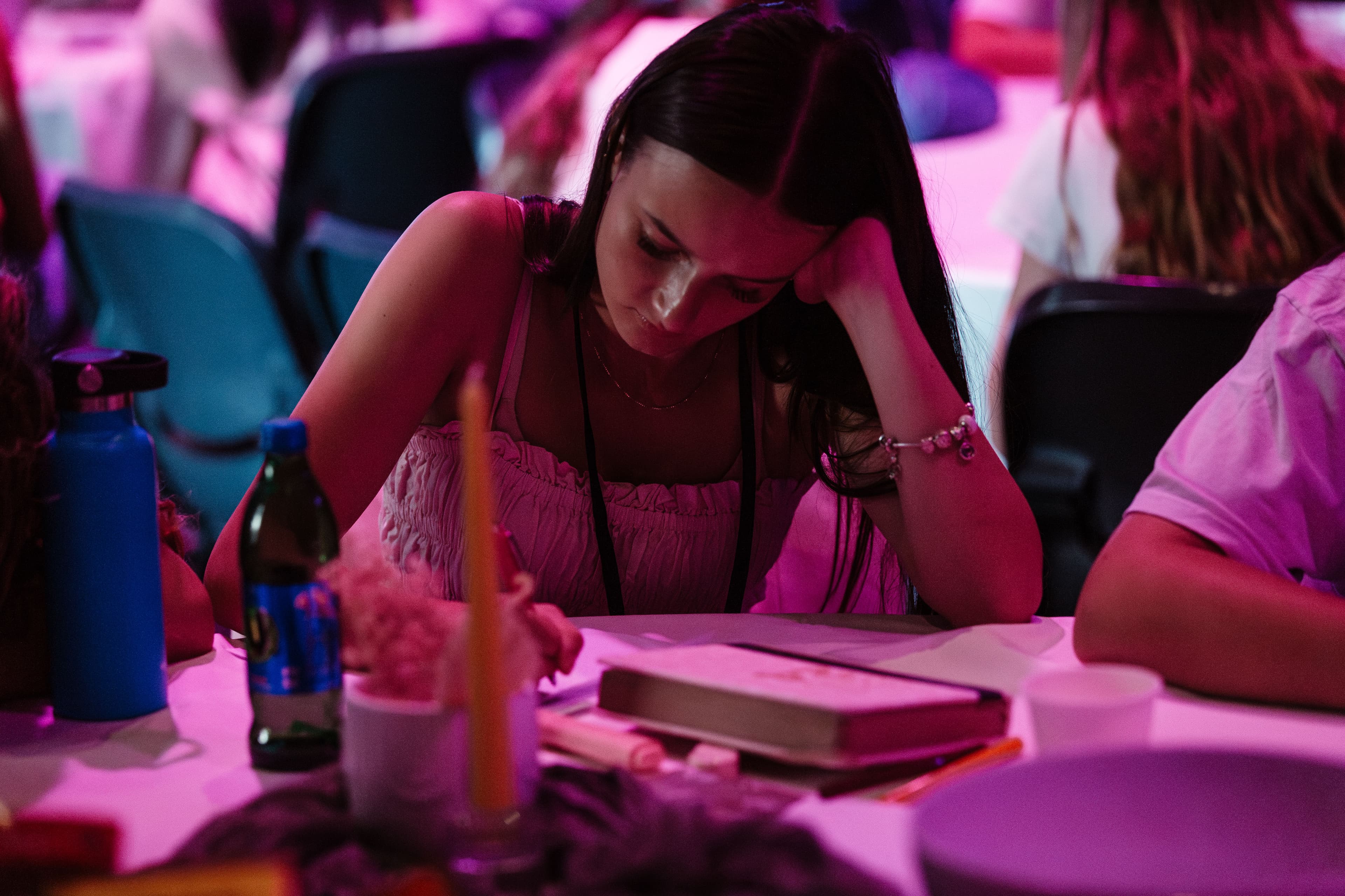 Young woman writing on a notebook her her hand holding her head up with pink light wash